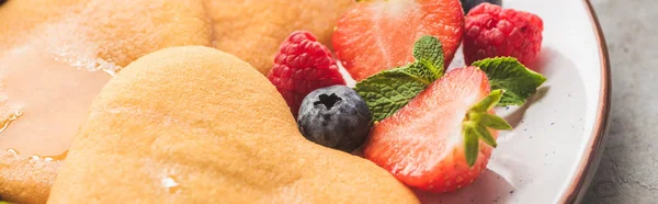 Vista de cerca de deliciosos panqueques en forma de corazón con bayas en el plato, plano panorámico - foto de stock