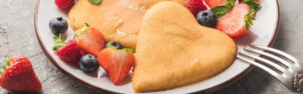 Vista de cerca de deliciosos panqueques en forma de corazón con bayas en el plato con tenedor, plano panorámico - foto de stock