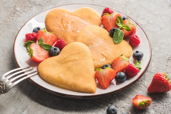 Deliciosas panquecas em forma de coração com bagas na placa com garfo na superfície de concreto cinza — Fotografia de Stock