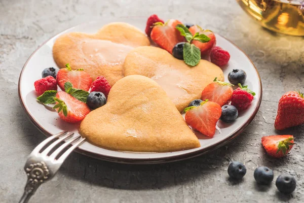 Deliciosas panquecas em forma de coração com bagas na placa com garfo na superfície de concreto cinza — Fotografia de Stock