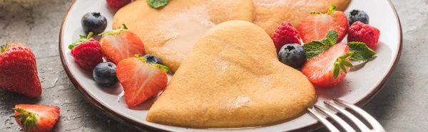 Deliziosi pancake a forma di cuore con bacche su piatto con forchetta su superficie di cemento grigio, colpo panoramico — Foto stock