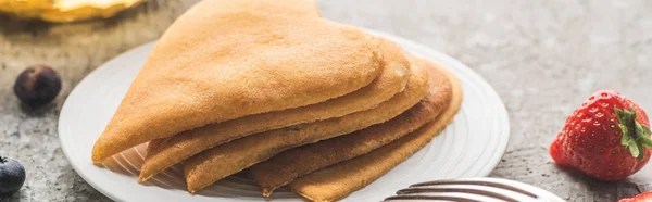 Deliziosi pancake a forma di cuore con bacche su piatto con forchetta su superficie di cemento grigio, colpo panoramico — Foto stock
