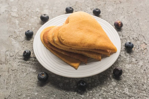 Delicious heart shaped pancakes on plate near blueberries on grey concrete surface — Stock Photo