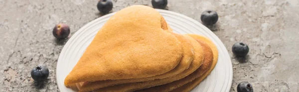 Leckere herzförmige Pfannkuchen auf Teller in der Nähe von Blaubeeren auf grauer Betonoberfläche, Panoramaaufnahme — Stockfoto