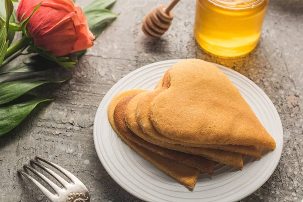 Heart shaped pancakes near honey, fork and rose on grey concrete surface — Stock Photo