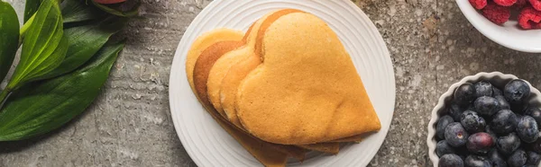 Top view of heart shaped pancakes with berries and rose on grey concrete surface, panoramic shot — Stock Photo