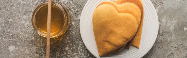 Top view of heart shaped pancakes near honey on grey concrete surface, panoramic shot — Stock Photo