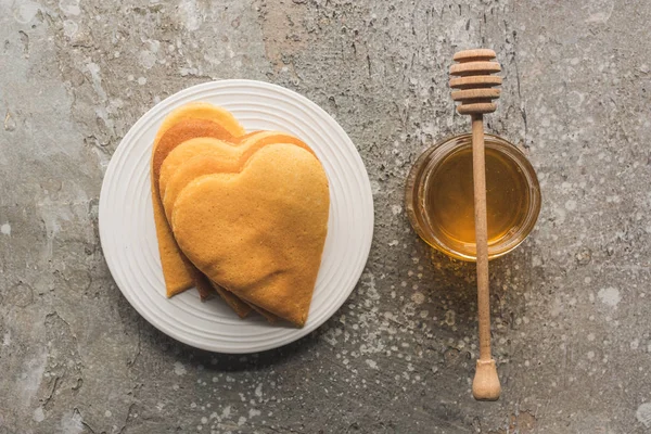 Top view of heart shaped pancakes near honey on grey concrete surface — Stock Photo