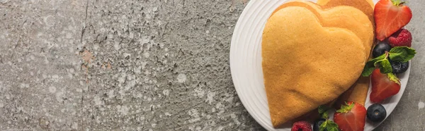 Vista dall'alto di frittelle a forma di cuore con bacche su una superficie di cemento grigio, colpo panoramico — Foto stock