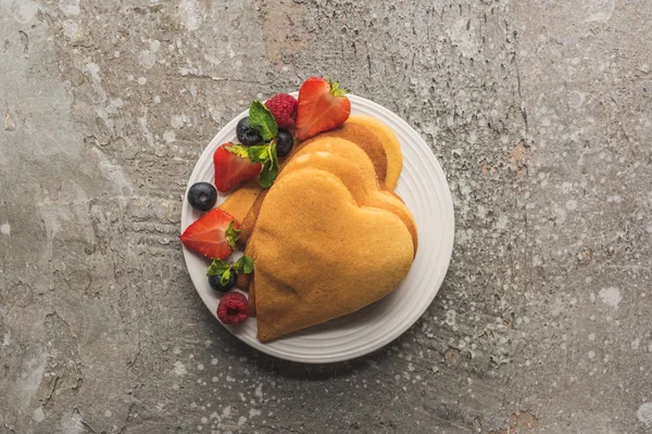 Vue de dessus des crêpes en forme de coeur avec des baies sur la surface en béton gris — Photo de stock