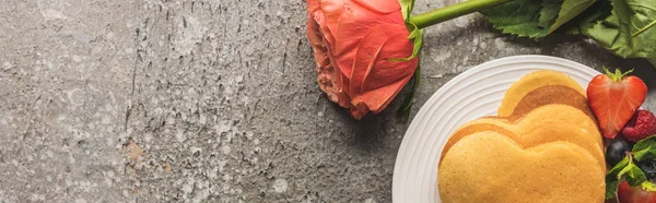 Draufsicht auf herzförmige Pfannkuchen mit frischen Beeren auf grauer Betonoberfläche mit Rose, Panoramaaufnahme — Stockfoto