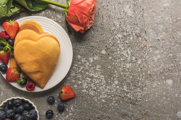 Top view of heart shaped pancakes with fresh berries on grey concrete surface with rose — Stock Photo