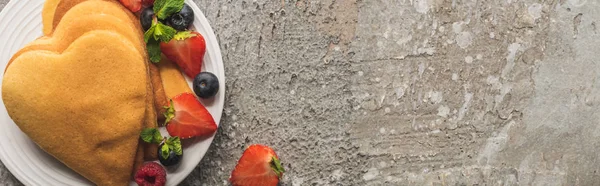 Vista dall'alto di frittelle a forma di cuore con gustose bacche sul piatto su una superficie di cemento grigio, colpo panoramico — Foto stock