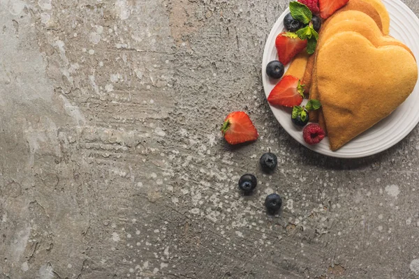 Vue de dessus des crêpes en forme de coeur avec de savoureuses baies sur plaque sur la surface en béton gris — Photo de stock