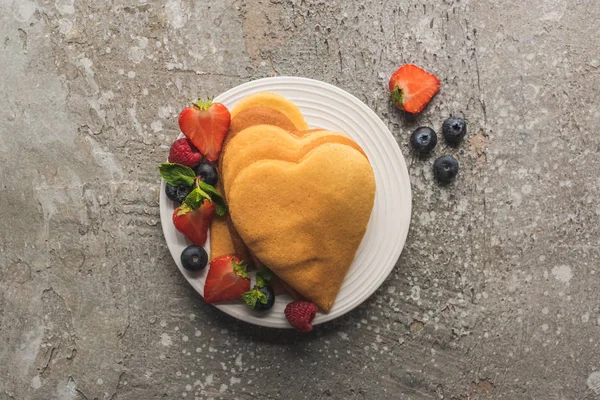 Vue de dessus des crêpes en forme de coeur avec de savoureuses baies sur plaque sur la surface en béton gris — Photo de stock