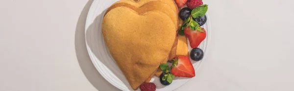 Vista dall'alto di frittelle a forma di cuore con gustose bacche su piatto su sfondo bianco, colpo panoramico — Foto stock