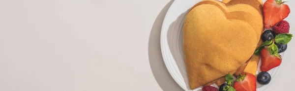 Draufsicht auf herzförmige Pfannkuchen mit leckeren Beeren auf Teller auf weißem Hintergrund, Panoramaaufnahme — Stockfoto