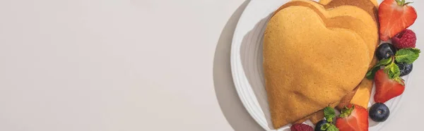 Vue de dessus des crêpes en forme de coeur avec de savoureuses baies sur fond blanc, vue panoramique — Photo de stock