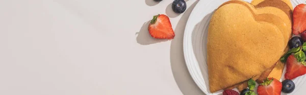 Top view of heart shaped pancakes with tasty berries on plate on white background, panoramic shot — Stock Photo