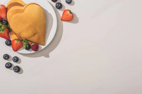Вид зверху на млинці у формі серця зі смачними ягодами на тарілці на білому фоні — стокове фото