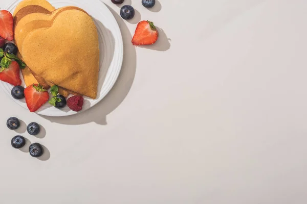 Vista superior de panqueques en forma de corazón con sabrosas bayas en el plato sobre fondo blanco - foto de stock