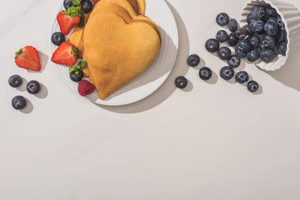 Top view of delicious heart shaped pancakes near scattered blueberries on white background — Stock Photo