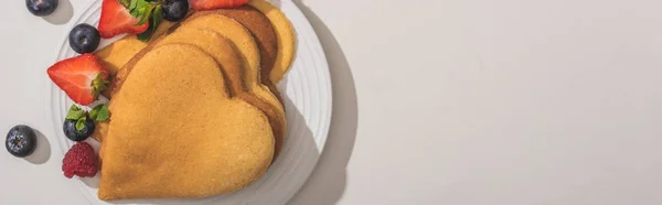 Vista dall'alto di deliziose frittelle a forma di cuore con bacche su sfondo bianco, colpo panoramico — Foto stock