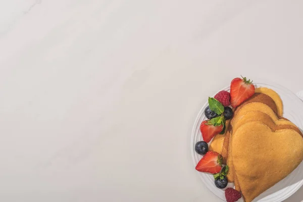 Draufsicht auf leckere herzförmige Pfannkuchen mit Beeren und Minze auf weißem Hintergrund — Stockfoto