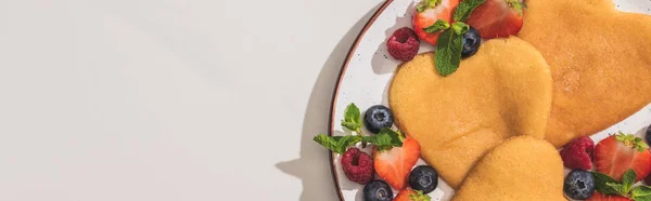 Draufsicht auf leckere herzförmige Pfannkuchen mit Beeren und Minze auf weißem Hintergrund, Panoramaaufnahme — Stockfoto