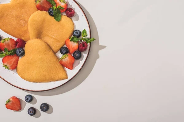 Vue de dessus des crêpes savoureuses en forme de coeur avec des baies et de la menthe sur fond blanc — Photo de stock