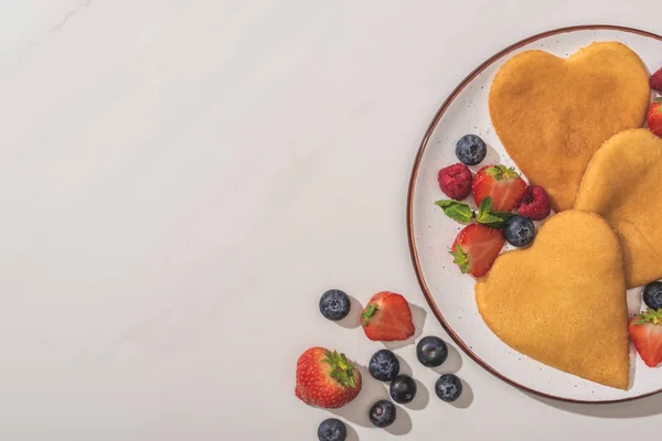 Draufsicht auf leckere herzförmige Pfannkuchen mit Beeren und Minze auf weißem Hintergrund — Stockfoto