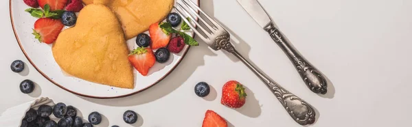 Top view of delicious heart shaped pancakes with berries near cutlery on white background, panoramic shot — Stock Photo