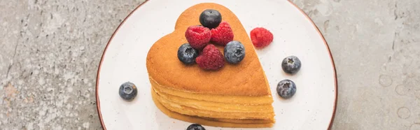 Tortitas en forma de corazón con bayas en placa sobre superficie de hormigón gris, plano panorámico - foto de stock