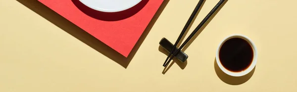 Top view of fresh nigiri with salmon near soy sauce and chopsticks on red and beige surface, panoramic shot — Stock Photo