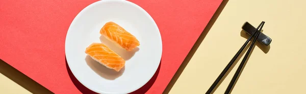 Top view of fresh nigiri with salmon near chopsticks on red and beige surface, panoramic shot — Stock Photo