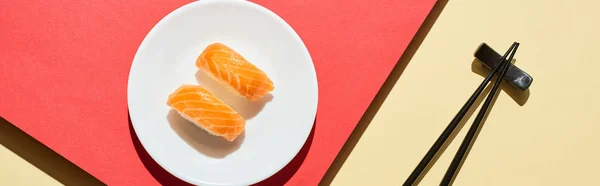 Vista dall'alto di nigiri freschi con salmone vicino a bacchette su superficie rossa e beige, colpo panoramico — Foto stock