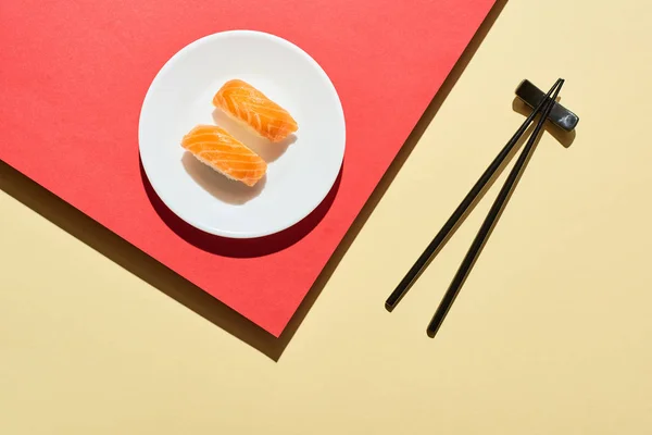 Vue de dessus du nigiri frais avec du saumon près des baguettes sur la surface rouge et beige — Photo de stock