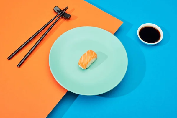 Fresh nigiri with salmon near soy sauce and chopsticks on blue and orange surface — Stock Photo