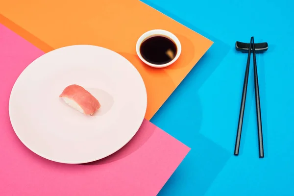 Fresh nigiri with tuna near soy sauce and chopsticks on pink, blue, orange surface — Stock Photo