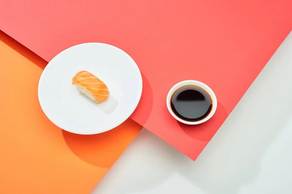 Fresh nigiri with salmon near soy sauce on red, orange, white surface — Stock Photo