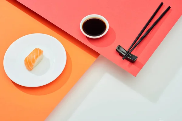 Nigiri fresco con salmón cerca de salsa de soja y palillos en la superficie roja, naranja, blanca - foto de stock