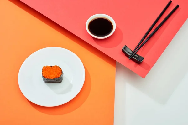 Nigiri frais au caviar rouge près de la sauce soja et baguettes sur surface rouge, orange, blanche — Photo de stock