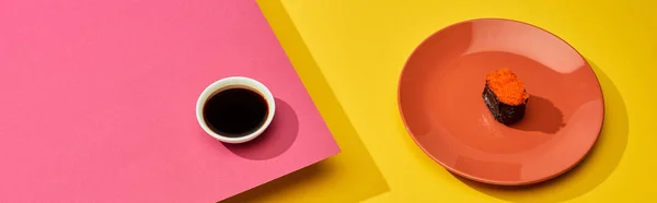 Maki fresco con caviale rosso su piatto vicino salsa di soia su rosa, superficie gialla, colpo panoramico — Foto stock