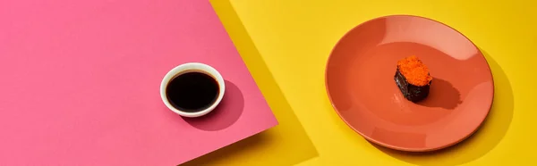 Fresh maki with red caviar on plate near soy sauce on pink, yellow surface, panoramic shot — Stock Photo