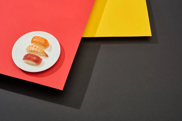 Nigiri fresco con salmón, camarones y atún sobre la superficie roja, amarilla y negra — Stock Photo