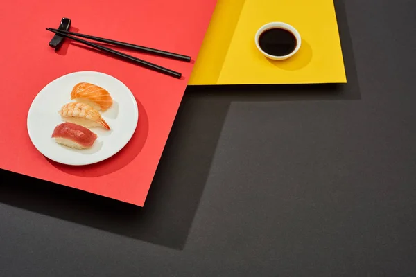 Fresh nigiri with salmon, shrimp and tuna near soy sauce and chopsticks on red, yellow and black surface — Stock Photo