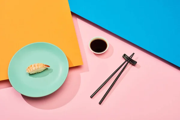 Fresh nigiri with shrimp near soy sauce and chopsticks on blue, pink, orange surface — Stock Photo