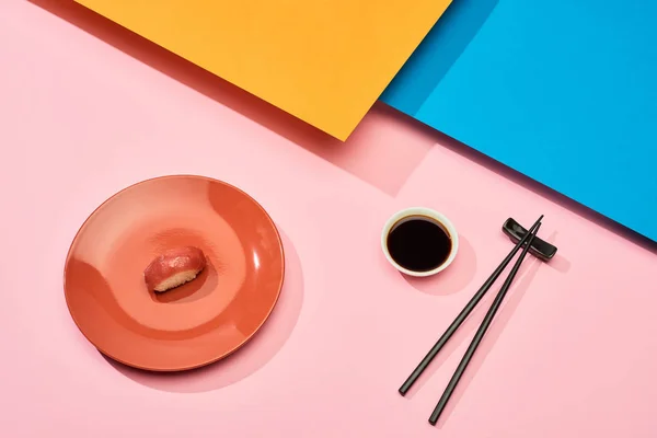 Свежий нигири с тунцом рядом с соевым соусом и палочками на голубой, розовой, оранжевой поверхности — стоковое фото