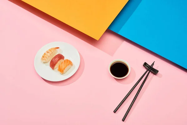 Nigiri fresco com salmão, atum e camarão perto de molho de soja e pauzinhos na superfície azul, rosa, laranja — Fotografia de Stock