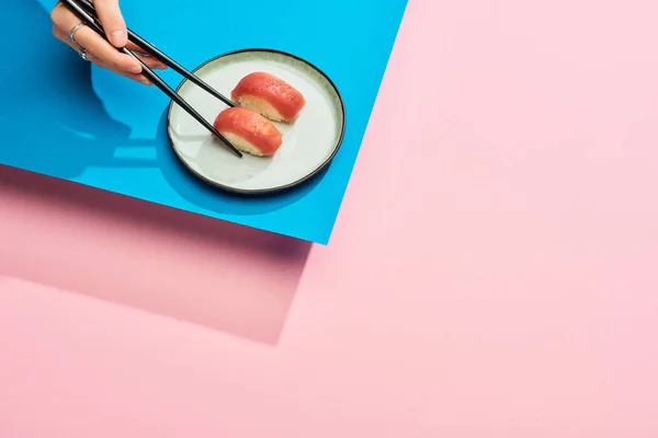 Partial view of woman eating fresh nigiri with tuna with chopsticks on blue, pink background — Stock Photo